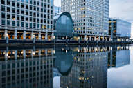 A modern building with a curved glass facade is reflected in the water.