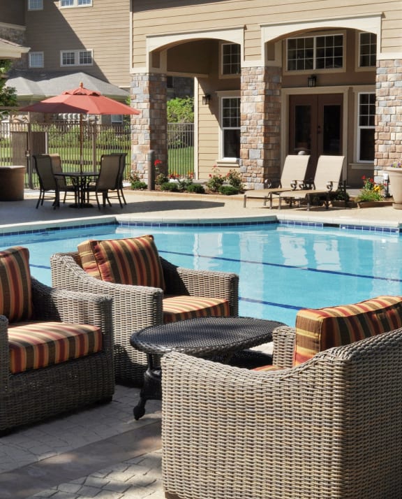 a swimming pool in front of a house with patio furniture