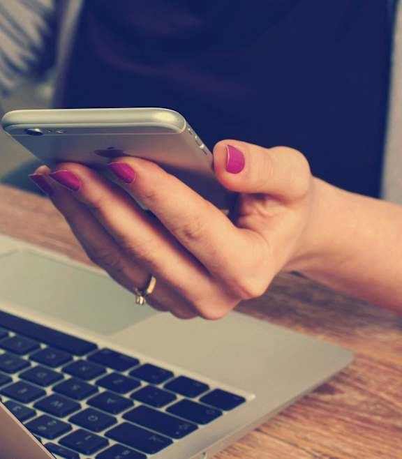 a woman holding a cell phone in front of a laptop computer