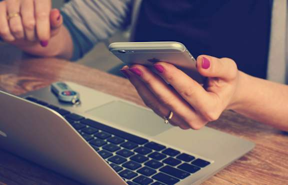 A person is using a smartphone while sitting at a laptop.