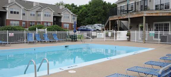 A swimming pool surrounded by blue lounge chairs and a white fence.