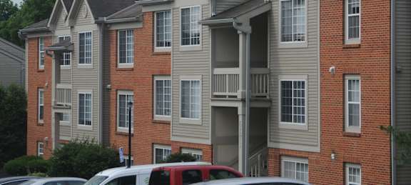 A red car is parked in front of a brick apartment building.