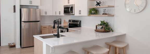 A modern kitchen with a white countertop and wooden stools.