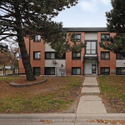 A red brick apartment building with a tree in front.