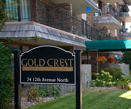 A sign for Gold Crest Apartments is in front of a building.