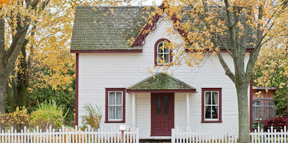 a small white house with a red door and a white picket fence in front of it
