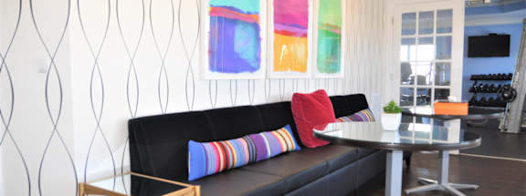 A black sofa with a red pillow and a glass table with a white tablecloth on it.