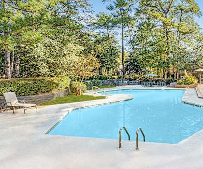 A large blue swimming pool surrounded by trees and a wooden deck.