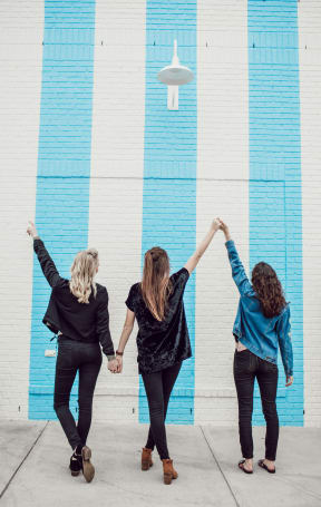 three women holding hands in front of a blue and white wall