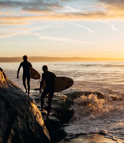 Two surfers are walking along the shore with their surfboards.