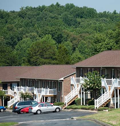A building with a brown roof and white railings is surrounded by trees.