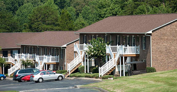 A building with a brown roof and white railings is surrounded by trees.