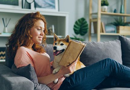 Woman sitting on couch with dog, reading