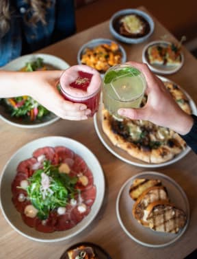 a person holding a drink over a table of plates of food