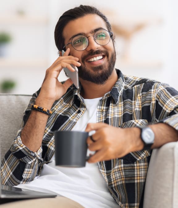 a man sitting on a couch talking on a cell phone with a laptop computer