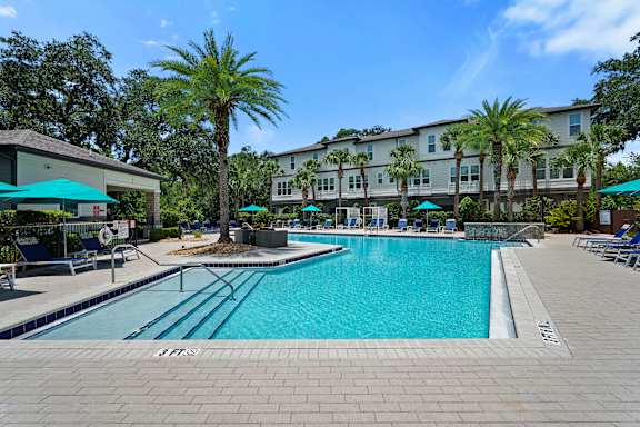 A large swimming pool surrounded by a brick patio and palm trees.
