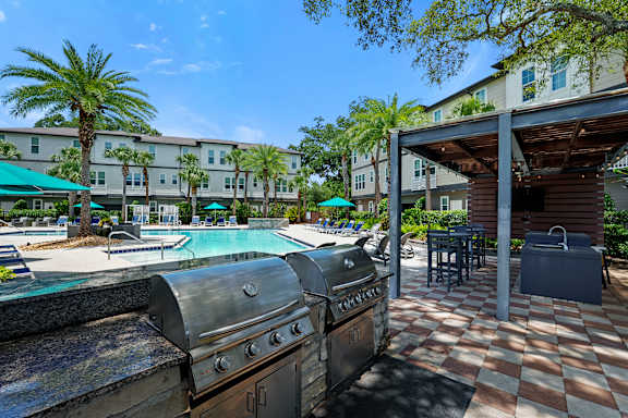 A BBQ grill is in the foreground of a resort style pool area.