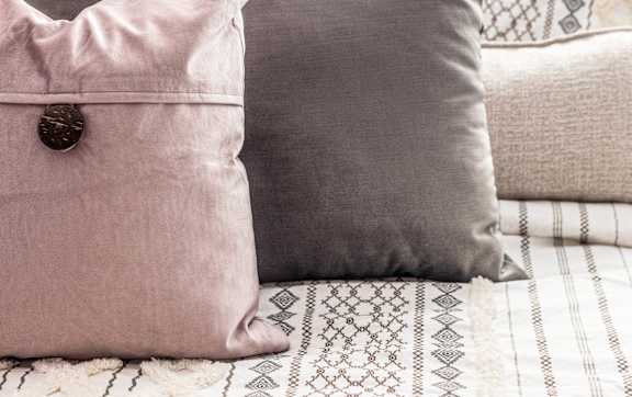 A pink pillow with a brown button sits on a bed.