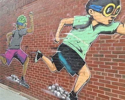 a painting of a man and a woman running on a brick wall at 1033 W Loyola, Chicago