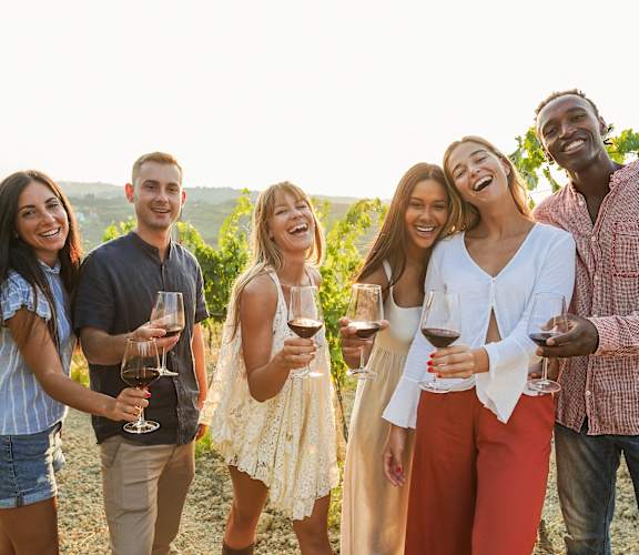 a group of people laughing and drinking wine in a vineyard