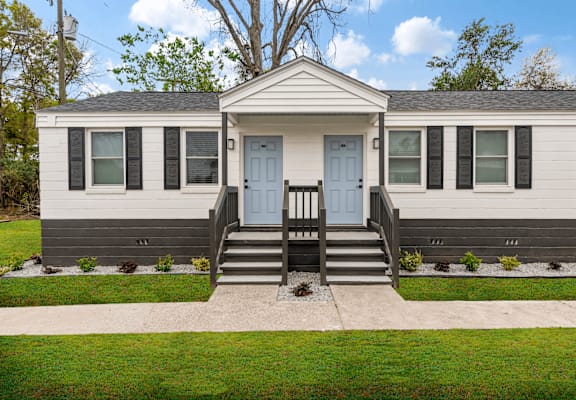 the front of a white house with blue doors and a porch