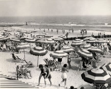 a black and white photo of a beach with people and umbrellas