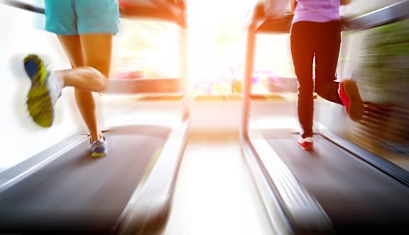 Two people running on treadmills in a brightly lit room.