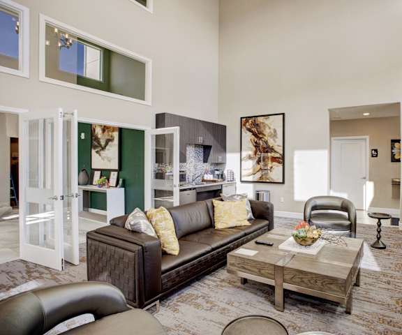 The community lounge with a leather couch, chairs, coffee tables, and a coffee bar, and a TV mounted on the wall at 600 Riverside. 