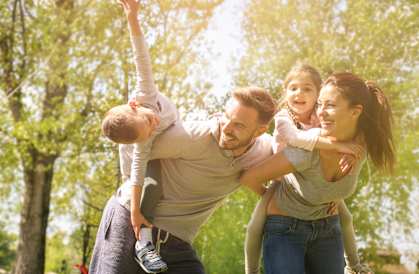 family of four piggyback with kids in park with trees