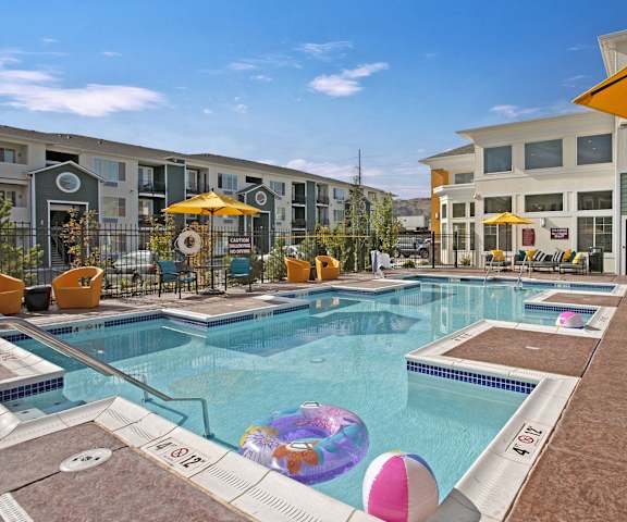 The pool at 600 Riverside with beach balls and an inner tube, and pool chairs and umbrellas surrounding it. 