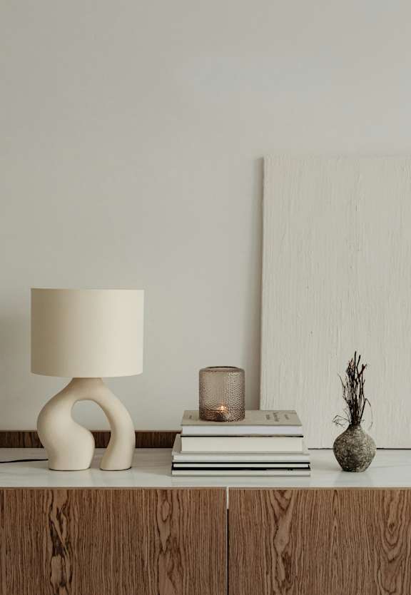 A table with a lamp, a candle, a vase, and a stack of books.