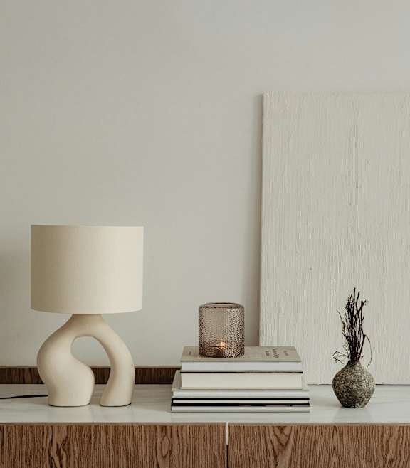 A table with a lamp, a candle, a vase, and a stack of books.