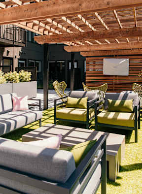 A patio with a white couch and green chairs.