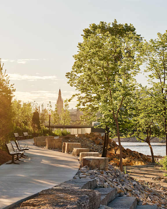 A park with a bench, trees, and a bridge over a river.