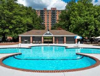 A large outdoor swimming pool surrounded by trees and a building in the background.
