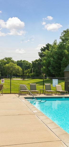 A pool with chairs around it and a blue sky with clouds. at Oakwood, Plymouth, MN, 55447