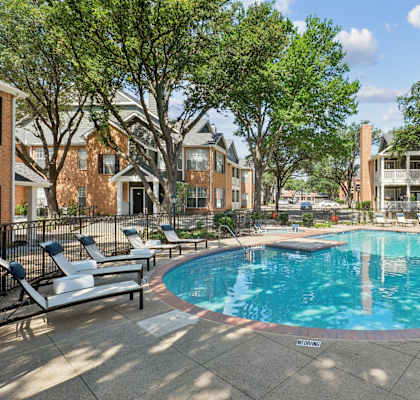 A swimming pool surrounded by trees and chairs in a residential area.