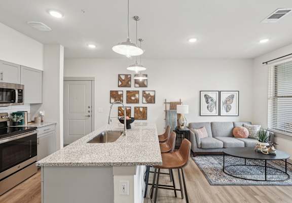 A modern kitchen with a granite countertop and a dining area with a grey couch.
