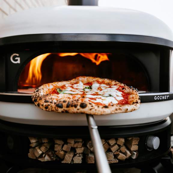 A pizza is being cooked in a white Gozey wood-fired oven.