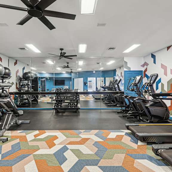 A gym with a variety of equipment including treadmills, elliptical machines, and a fan.