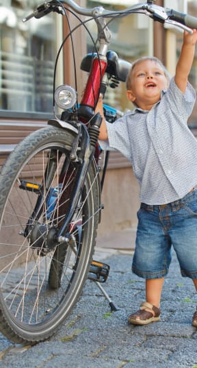 a little boy holding up his bike on a street