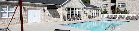 A large orange umbrella is shading a table and chairs by a pool.