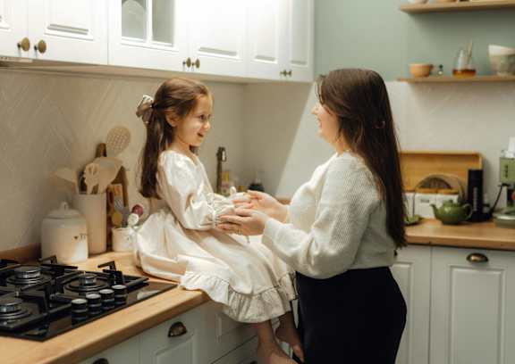 A woman and a little girl are standing in a kitchen.