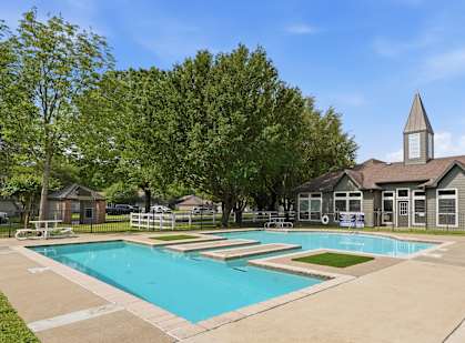A large swimming pool surrounded by a concrete patio and a small building with a steeple.