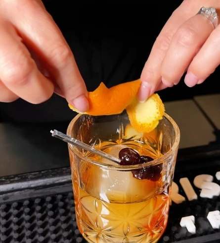 A person is squeezing an orange peel into a glass of a drink.