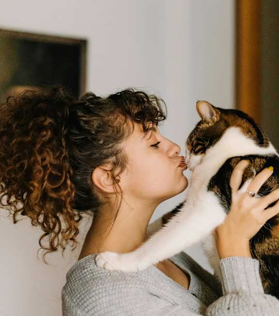 A woman with curly hair is wearing a grey sweater and holding a cat.