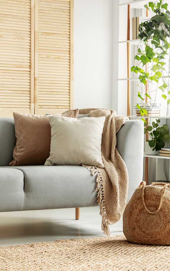 A cozy living room with a grey couch, a beige throw blanket, and a woven bag on a woven rug.