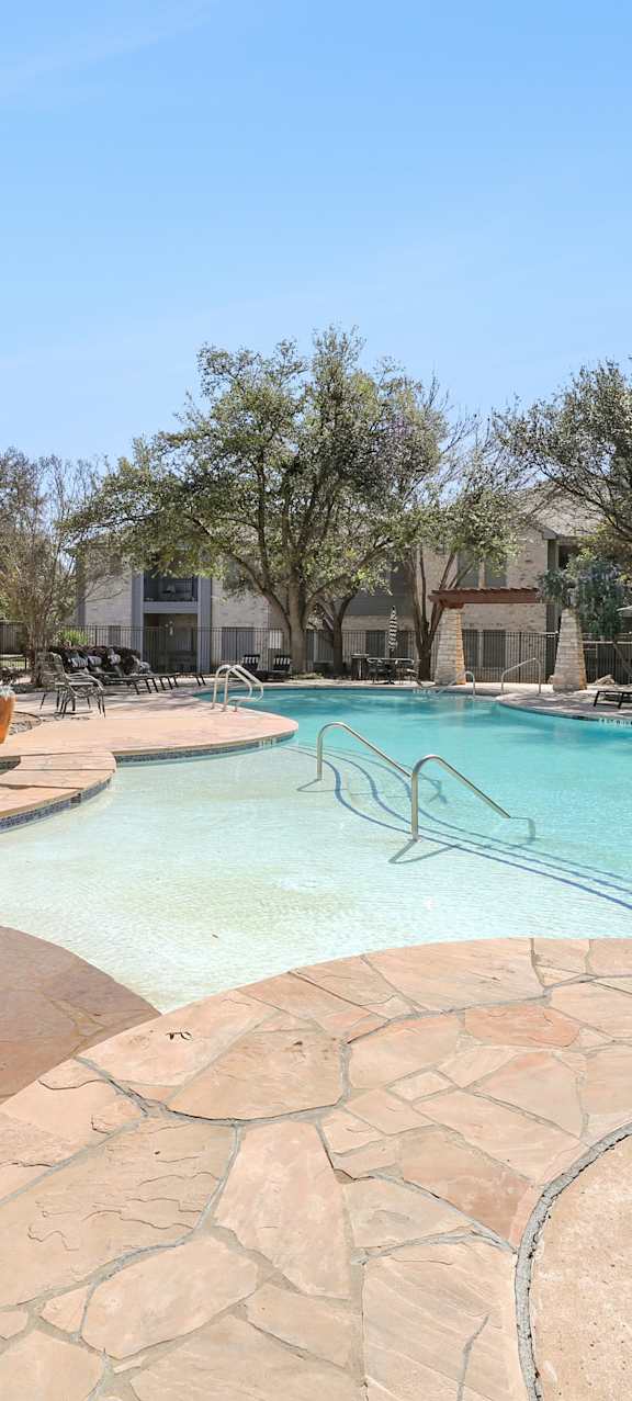 A large outdoor swimming pool surrounded by a stone patio.