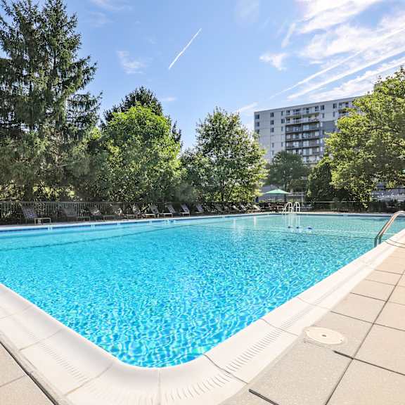 A large swimming pool surrounded by trees and a building in the background.