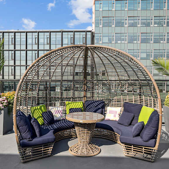 A wicker sofa with cushions and a table is set up on a rooftop.